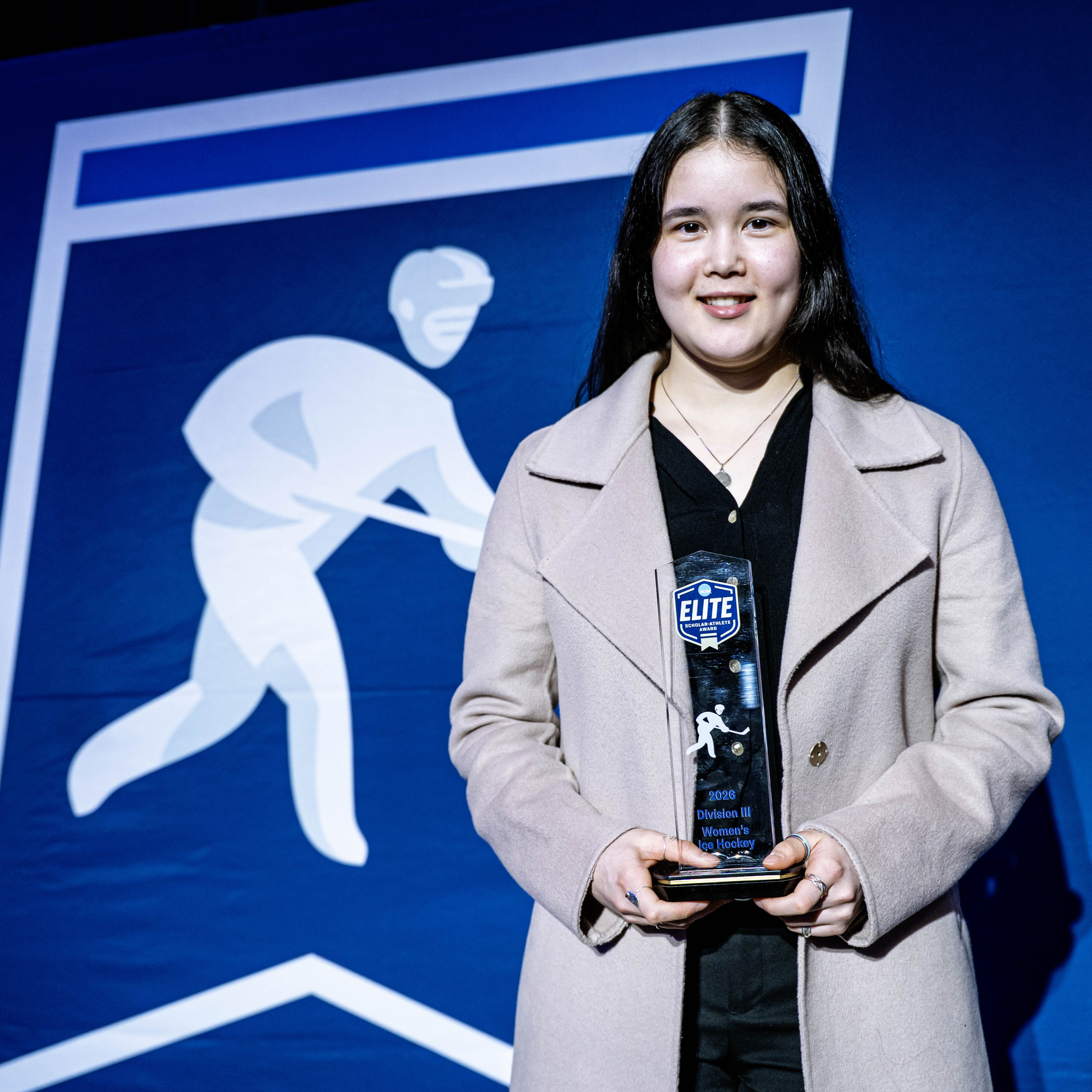 Person holds an Elite award in front of a blue ice hockey banner.