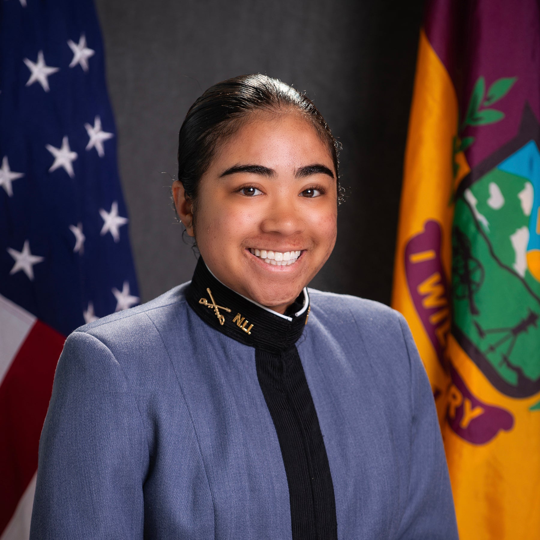Cadet in dress uniform poses for a portrait between U.S. and Norwich University flags.