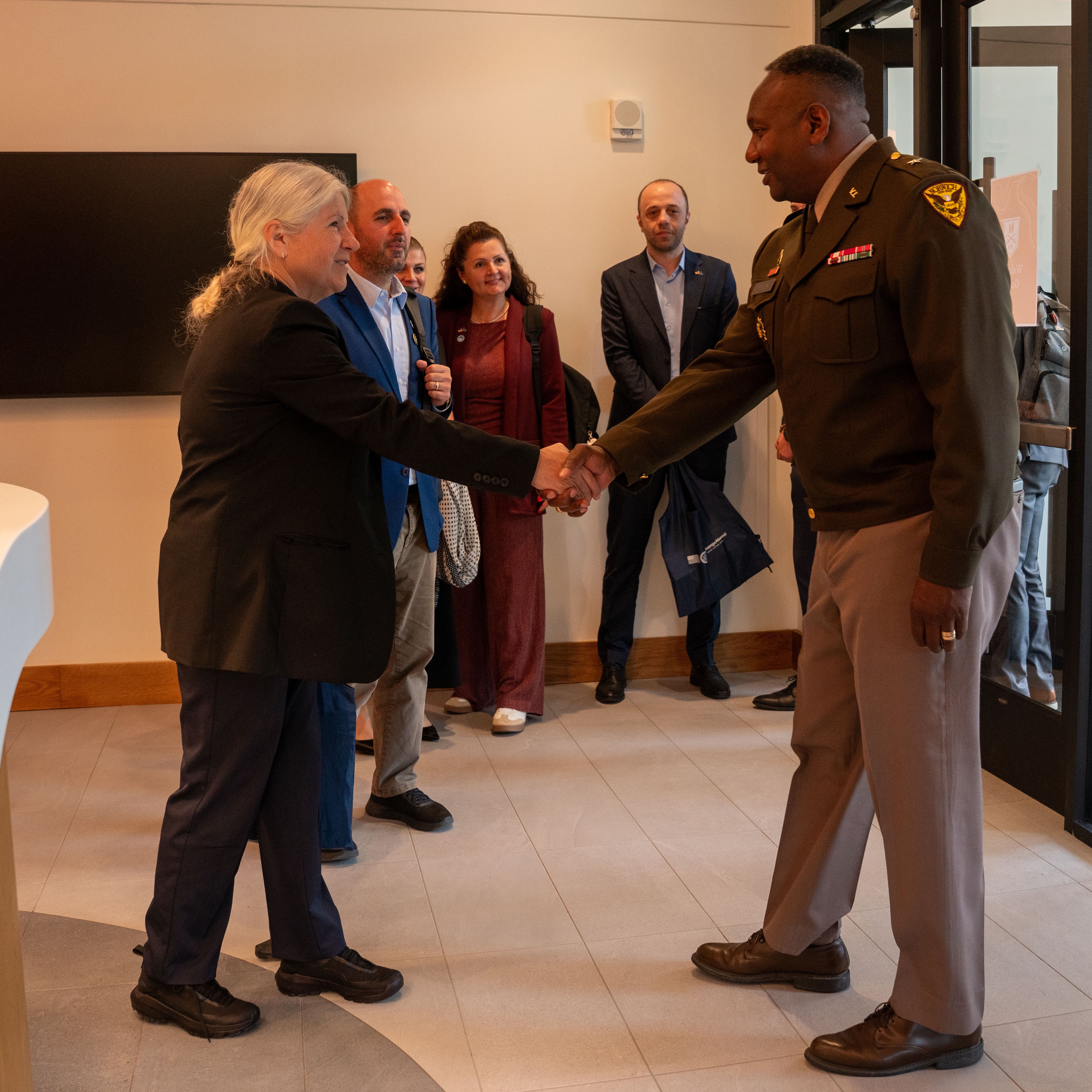 A service member shakes hands with a person as others watch.
