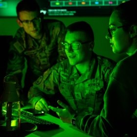 Three students in front of a computer in the Norwich University Cyber War Room.