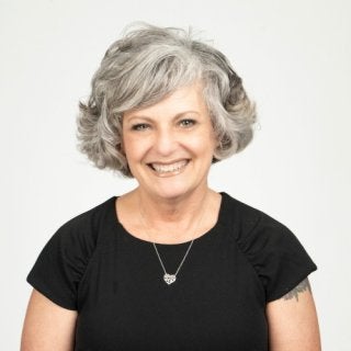 Individual in black blouse wearing a necklace. Headshot photo of Teri-Gene Conlin against a white background