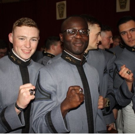 Group of cadets in uniform showing their rings at a formal event.