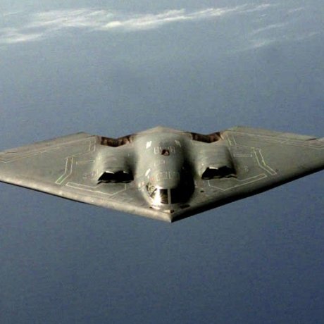 A B-2 Spirit stealth bomber in flight against a cloudy sky.