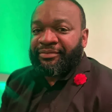 raheem Berry in a black shirt and suit portrait style.