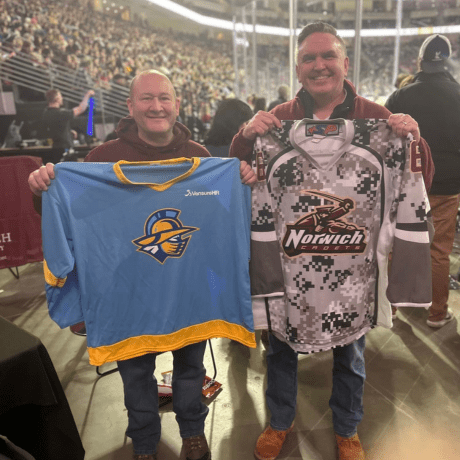 An image of two NU Alumni holding hockey jerseys, for the Atlanta Gladiators and the Norwich Cadets