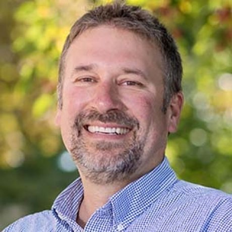 A headshot of a smiling man outdoors.