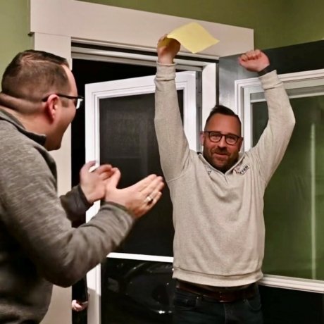 a man in foreground, facing another man with hands in air, holding a paper ballot