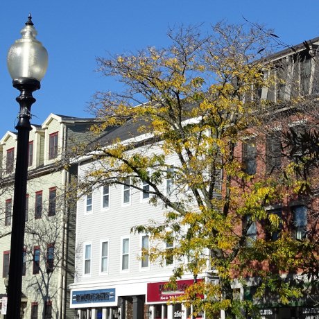 Three buildings are seen behind an older street lamp. "Architectural Detail - West Broadway - South Boston - MA - USA - 02 (52485266226)" by Adam Jones from Kelowna, BC, Canada is licensed under CC BY 2.0.