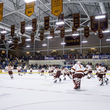 Norwich hockey players skate across the ice as fans stand behind the boards under championship banners.
