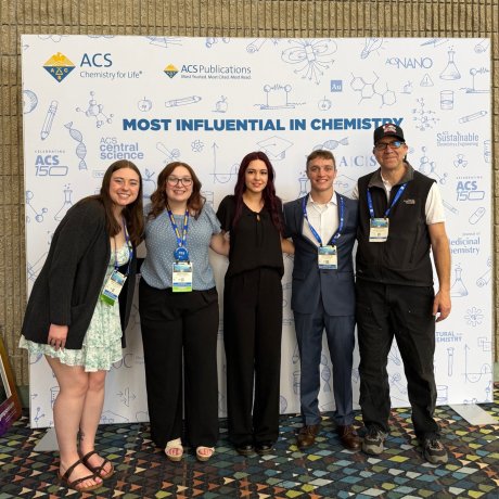 Five people pose with conference badges in front of an ACS Chemistry for Life backdrop.
