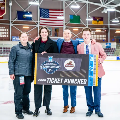 Four people pose on the ice holding a Norwich 2026 NCAA Women's Hockey Championship Ticket Punched sign.