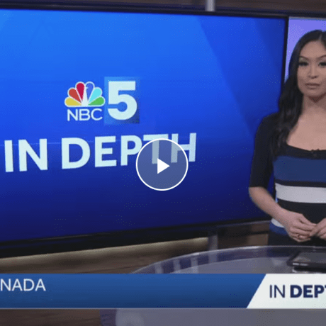 TV news anchor stands beside an NBC5 In Depth screen in a studio.