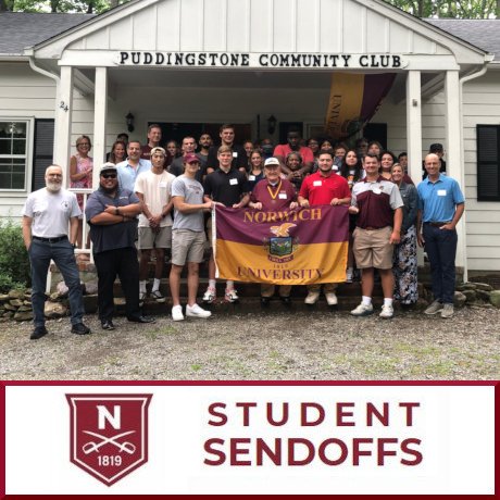 A large group of individuals stand at the entrance to a building with sign: Puddingstone Community Club.  Five individuals center front hold up a maroon and gold flag for Norwich University.