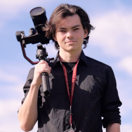Student holds camera stabilizer outdoors while wearing a Norwich University lanyard.