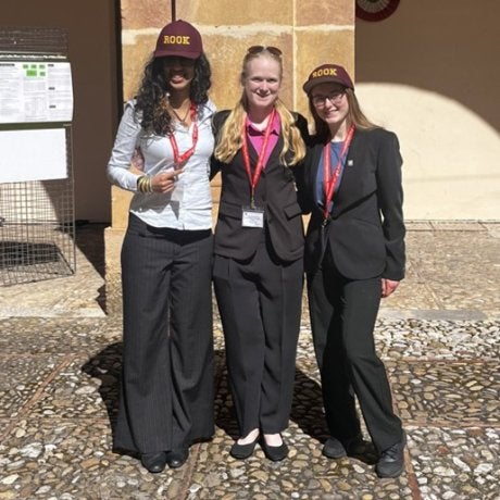Three students wearing ROOK hats and conference badges stand in front of a stone column outdoors.