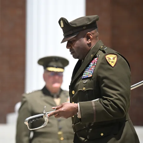Uniformed officer holds a ceremonial sword during an outdoor military ceremony.