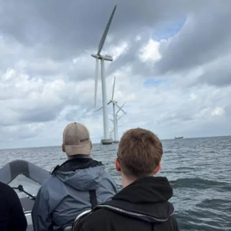 Two people ride in a boat toward offshore wind turbines.