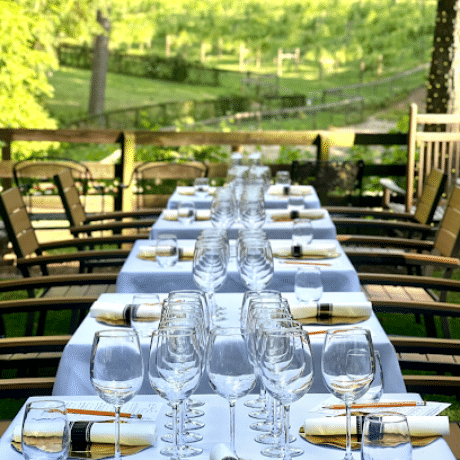 A table setting with several wine glasses and numerous place settings on tables with white table cloths and chairs.