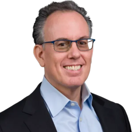 Portrait of a person wearing glasses, a dark blazer, and a light blue collared shirt.