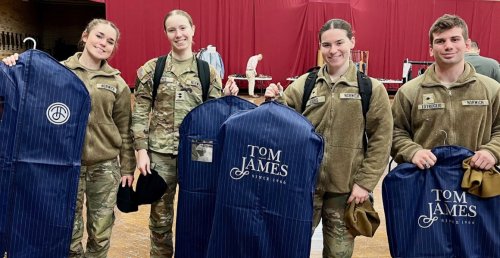 A group of Norwich cadets in olive / camo uniform hold blue garment bags with wording Tom James on bag reverse. 