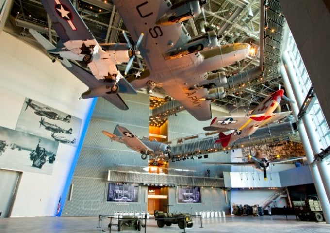 Aircraft hang from the ceiling of a museum gallery, with historic aircraft displays and exhibit panels below.
