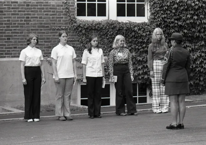 Female freshmen ("rooks") in line facing an individual in formal military dress on Norwich University's Upper Parade Ground during student orientation or "Rook Week" in September 1974.