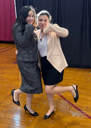 Two women standing beside each other, both with one foot off the floor and holding their arms at an angle. They are both wearing formal wear donated to them through Dressing for Success, held Feb. 9-10 at Norwich University.