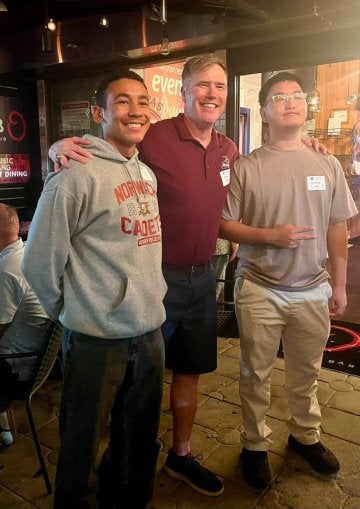 An older individual in red polo shirt stands between two younger individuals.
