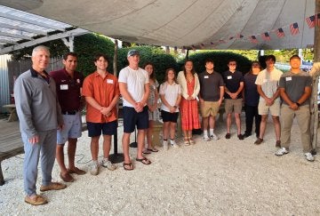 Twelve individuals stand below an outdoor event tent.