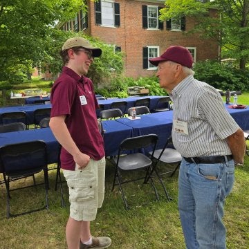 Two individuals are talking to each other in front of a blue-covered table and metal folding chairs.